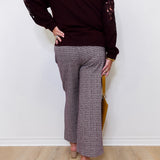 Person wearing a dark brown sweater with lace sleeves and patterned pants against a white wall.