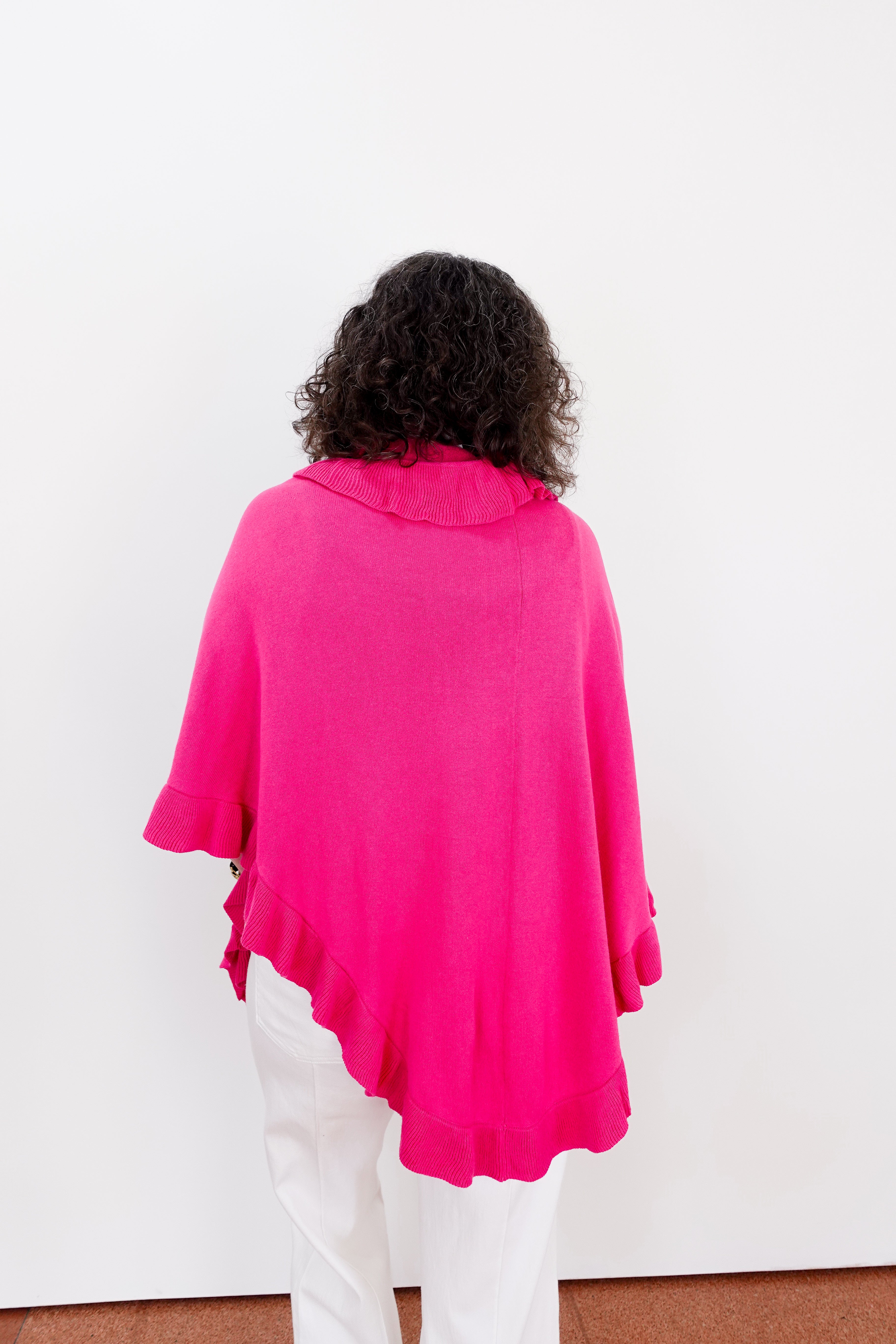 Person wearing a bright pink poncho over a white outfit on a plain background