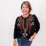 Woman wearing a black embroidered top with colorful designs on a white background