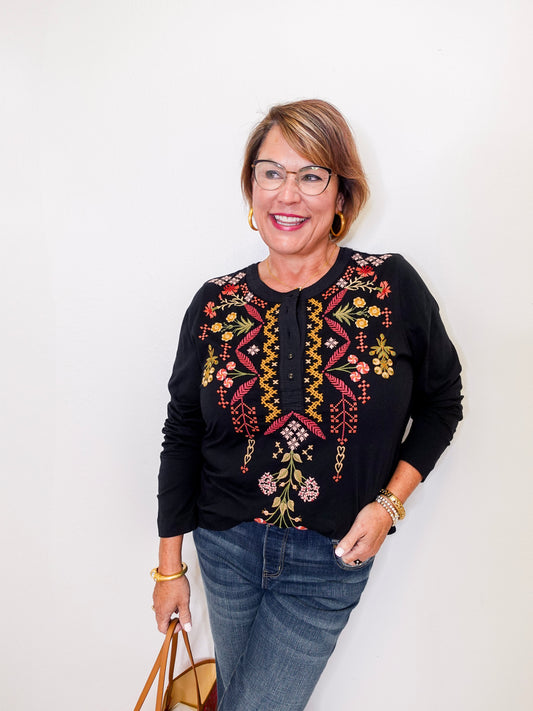 Woman wearing a black embroidered top with colorful designs on a white background