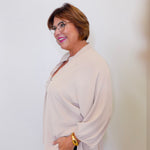 Woman wearing a beige blouse and black pants against a white background