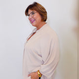 Woman wearing a beige blouse and black pants against a white background