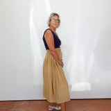 Woman wearing a navy top and beige skirt standing against a white wall.