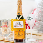 Veuve Clicquot champagne bottle with a decorative label on a table with a glass and other items.