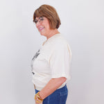 Woman wearing a white blouse with a graphic design and blue jeans against a plain background