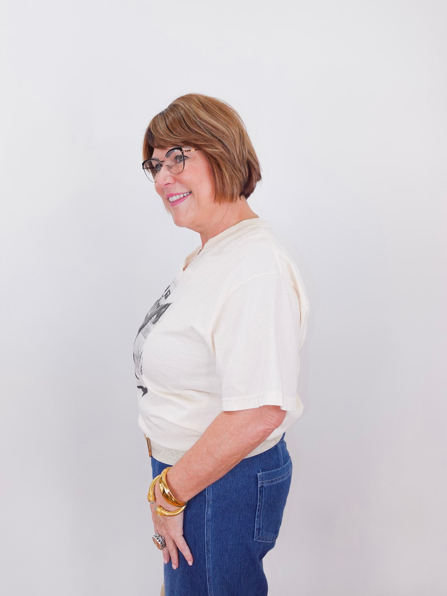 Woman wearing a white blouse with a graphic design and blue jeans against a plain background