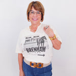 Woman wearing a white t-shirt with a graphic design and text, standing against a plain background.