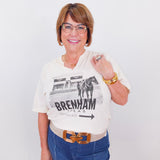 Woman wearing a white t-shirt with a graphic design and text, standing against a plain background.