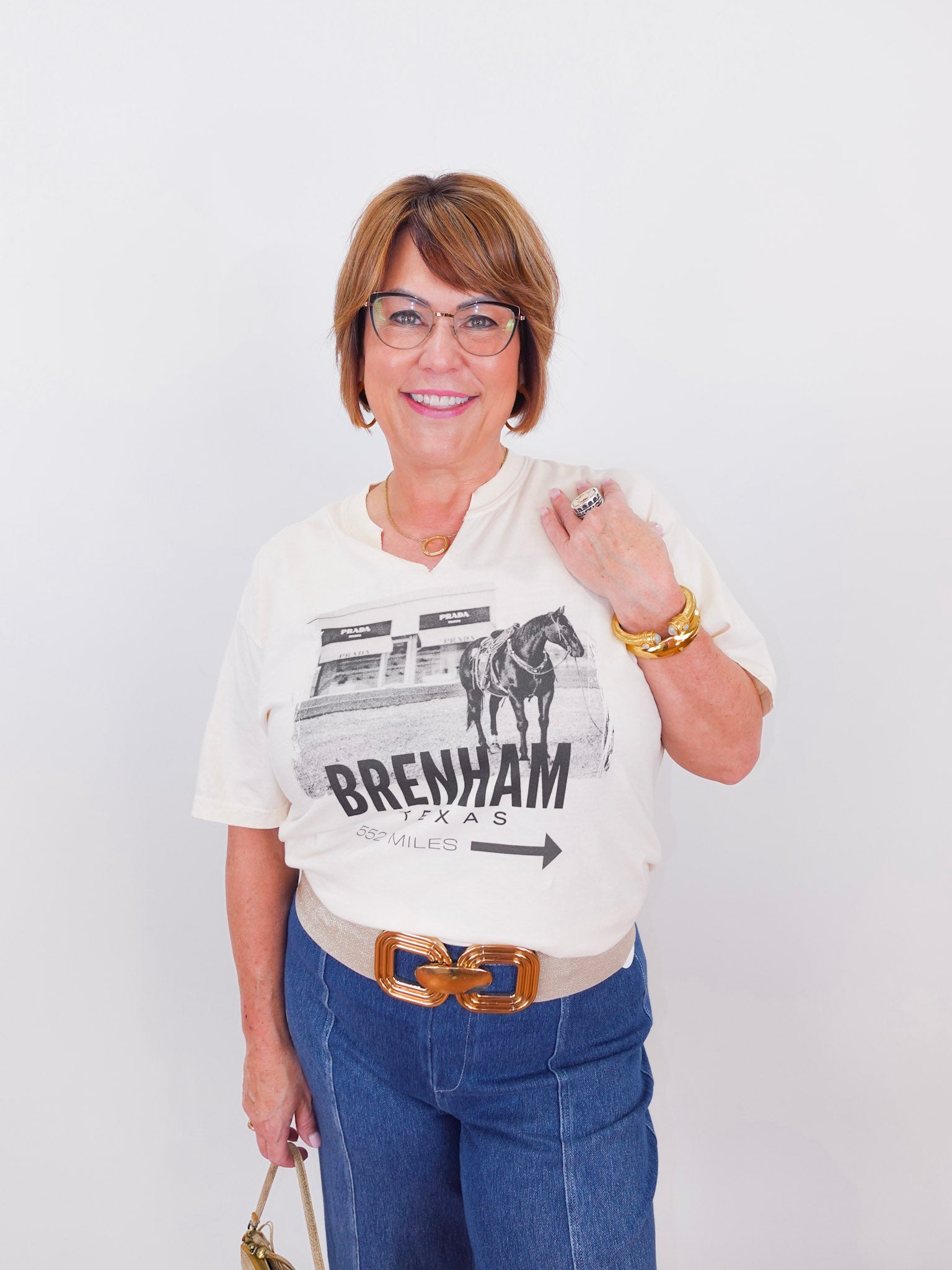 Woman wearing a white t-shirt with a graphic design and text, standing against a plain background.