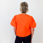 Person wearing an orange blouse with puff sleeves on a white background