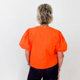 Person wearing an orange blouse with puff sleeves on a white background