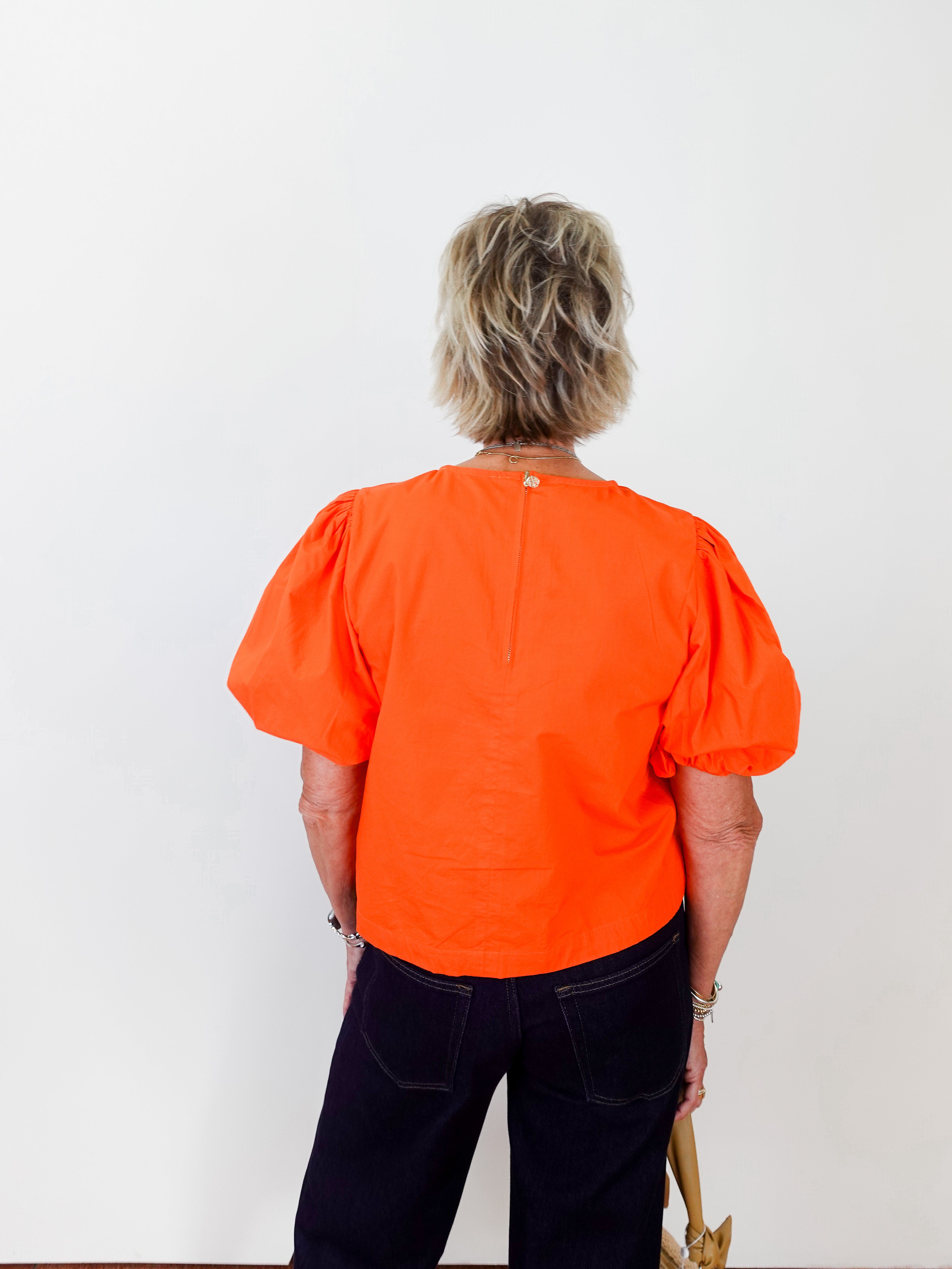 Person wearing an orange blouse with puff sleeves on a white background