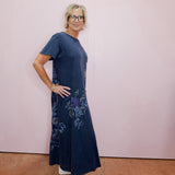 Woman wearing a navy blue dress with floral embroidery against a pink wall.