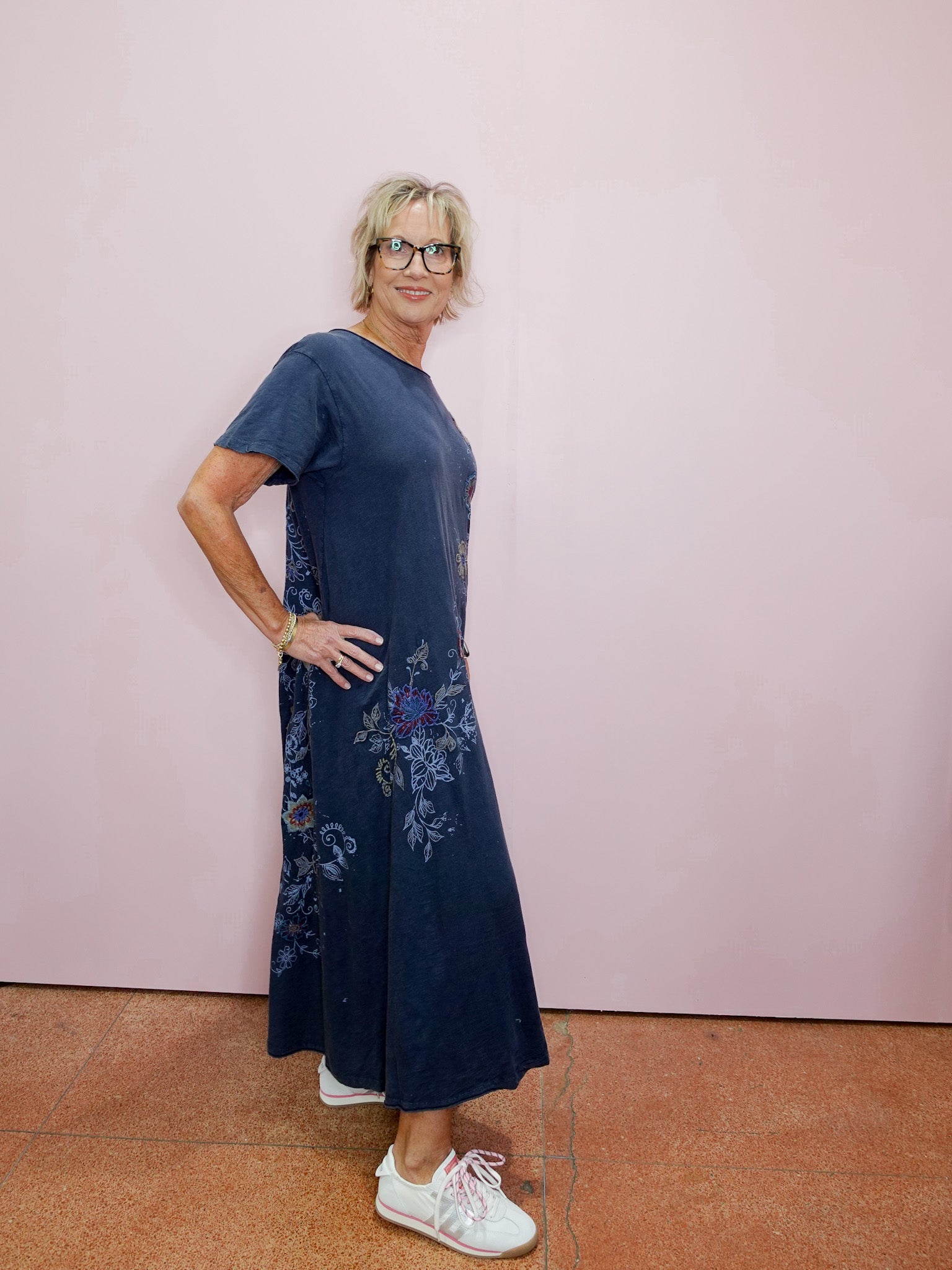 Woman wearing a navy blue dress with floral embroidery against a pink wall.
