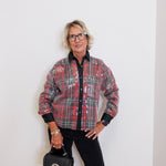 Person wearing a plaid shirt and holding a black handbag against a white background