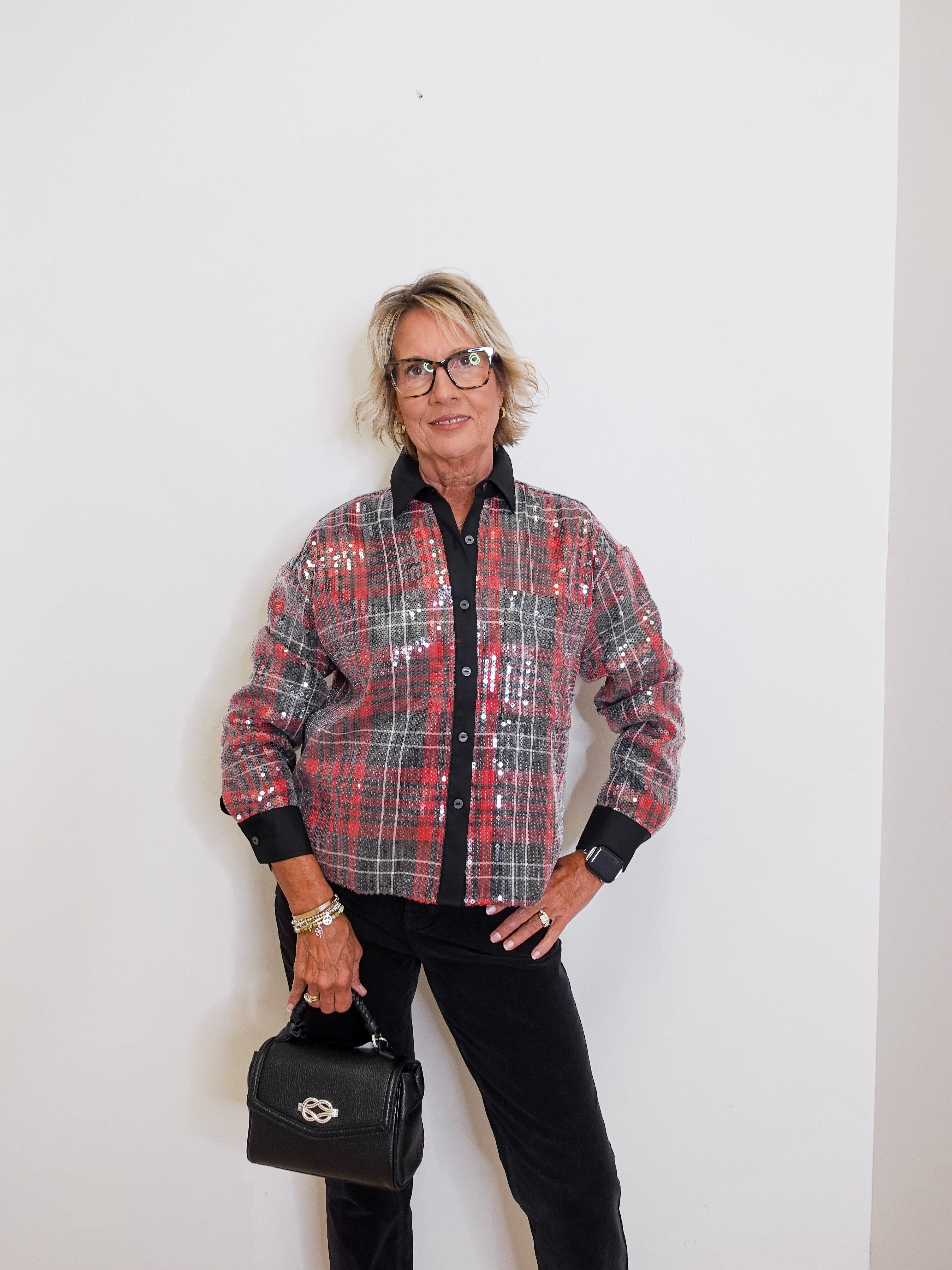 Person wearing a plaid shirt and holding a black handbag against a white background