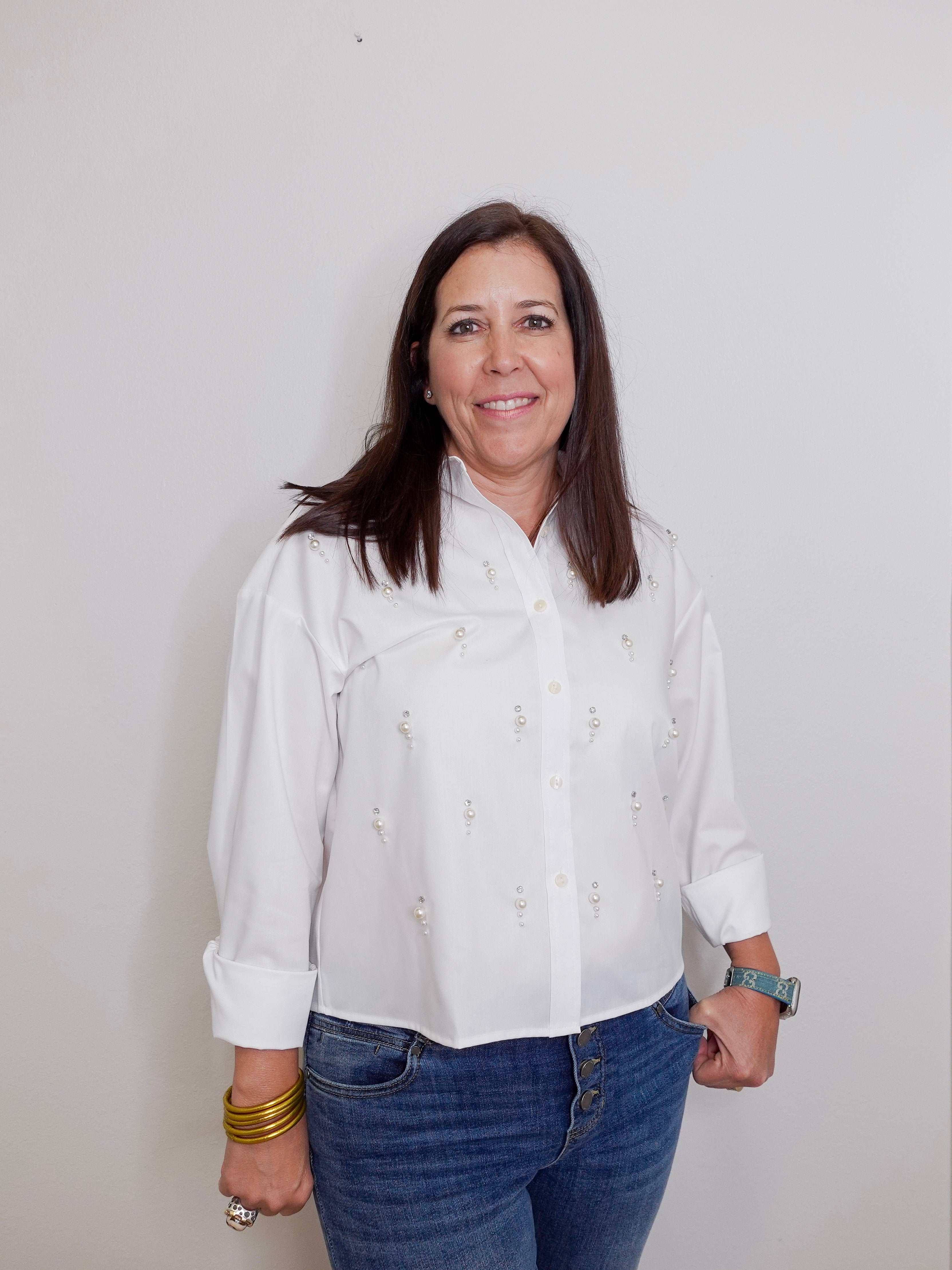 Woman wearing a white blouse and blue jeans against a plain background