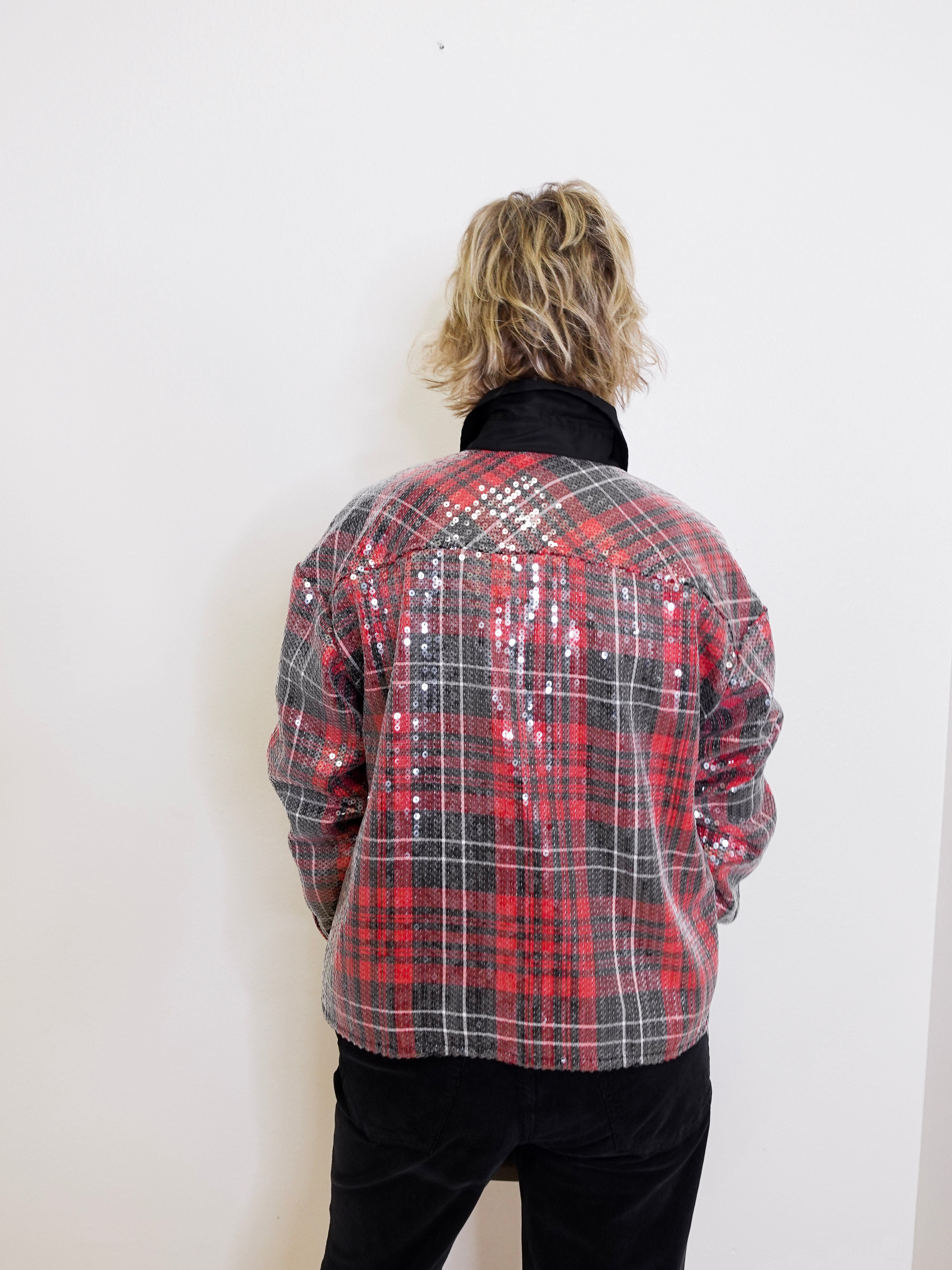 Person wearing a red and black plaid jacket with sequin details on a white background