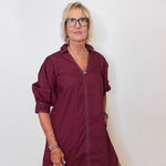 Woman wearing a burgundy dress with rolled-up sleeves against a white background