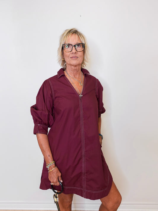 Woman wearing a burgundy dress with rolled-up sleeves against a white background