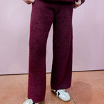 Person wearing a maroon outfit with white shoes on a pink floor.