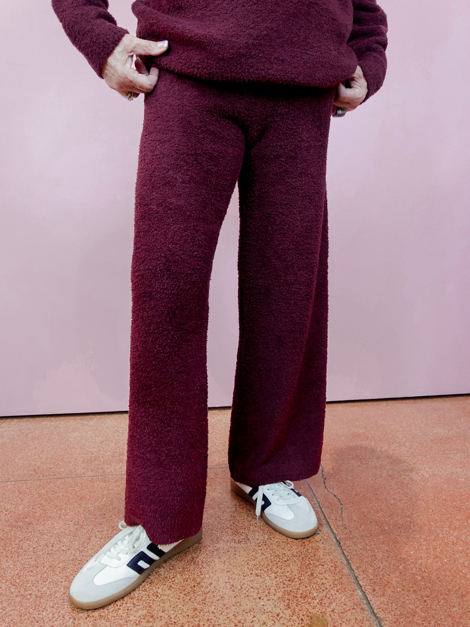 Person wearing a maroon outfit with white shoes on a pink floor.