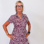 Woman wearing a patterned dress and glasses against a white background