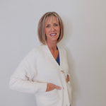 A person wearing a white crop cardigan with long sleeves against a white background. 