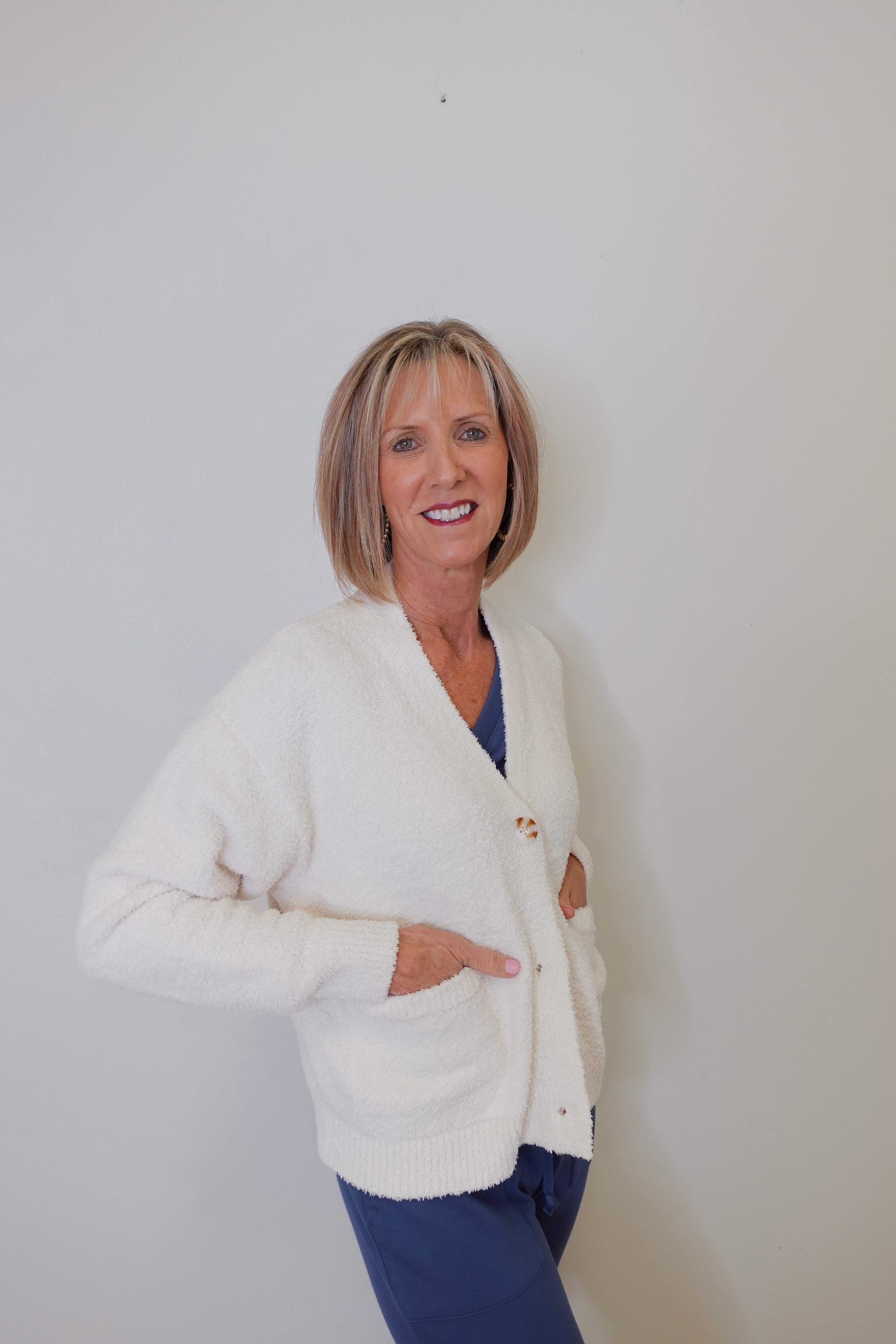A person wearing a white crop cardigan with long sleeves against a white background. 