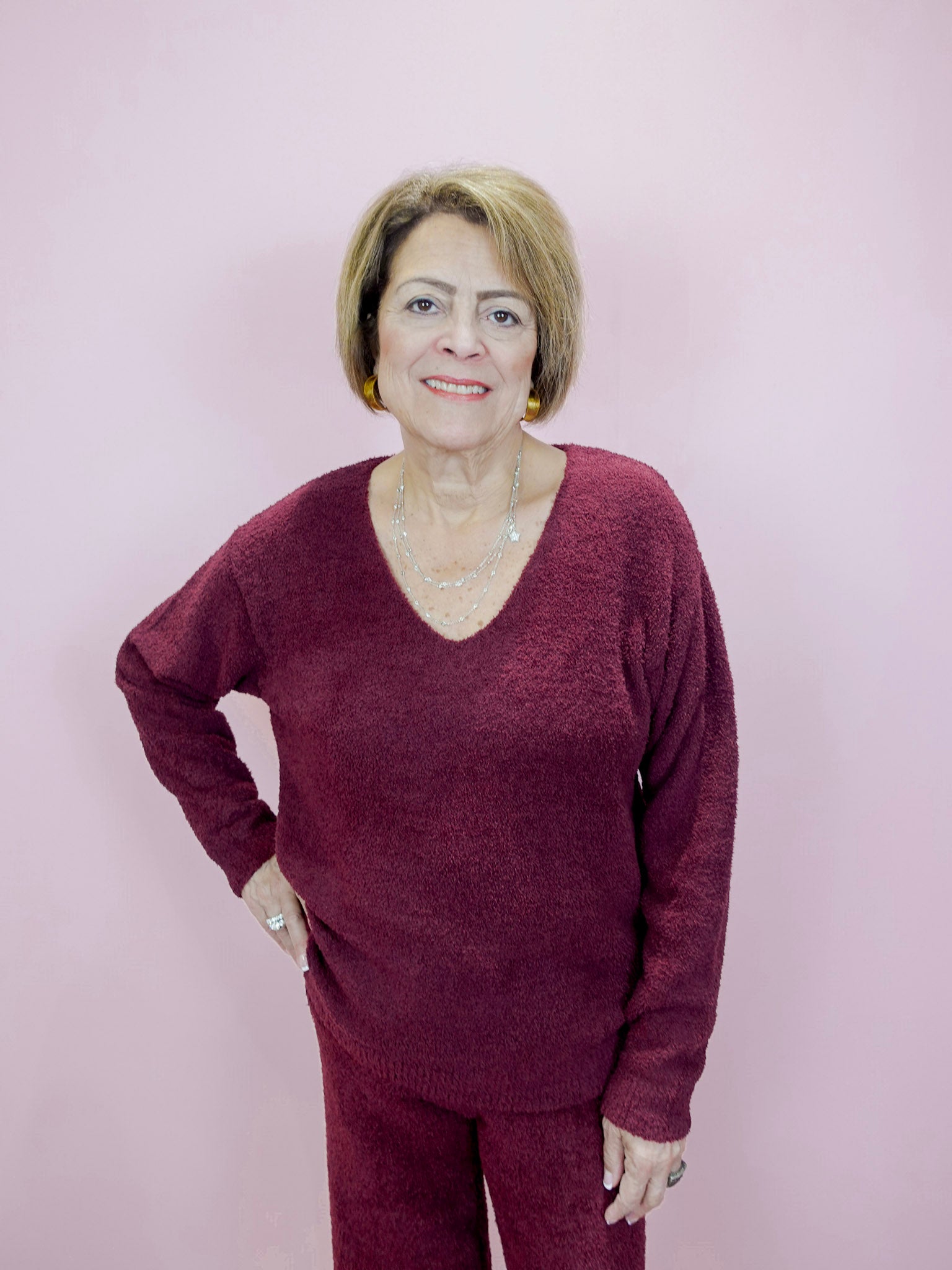Woman wearing a maroon sweater and pants against a light pink background