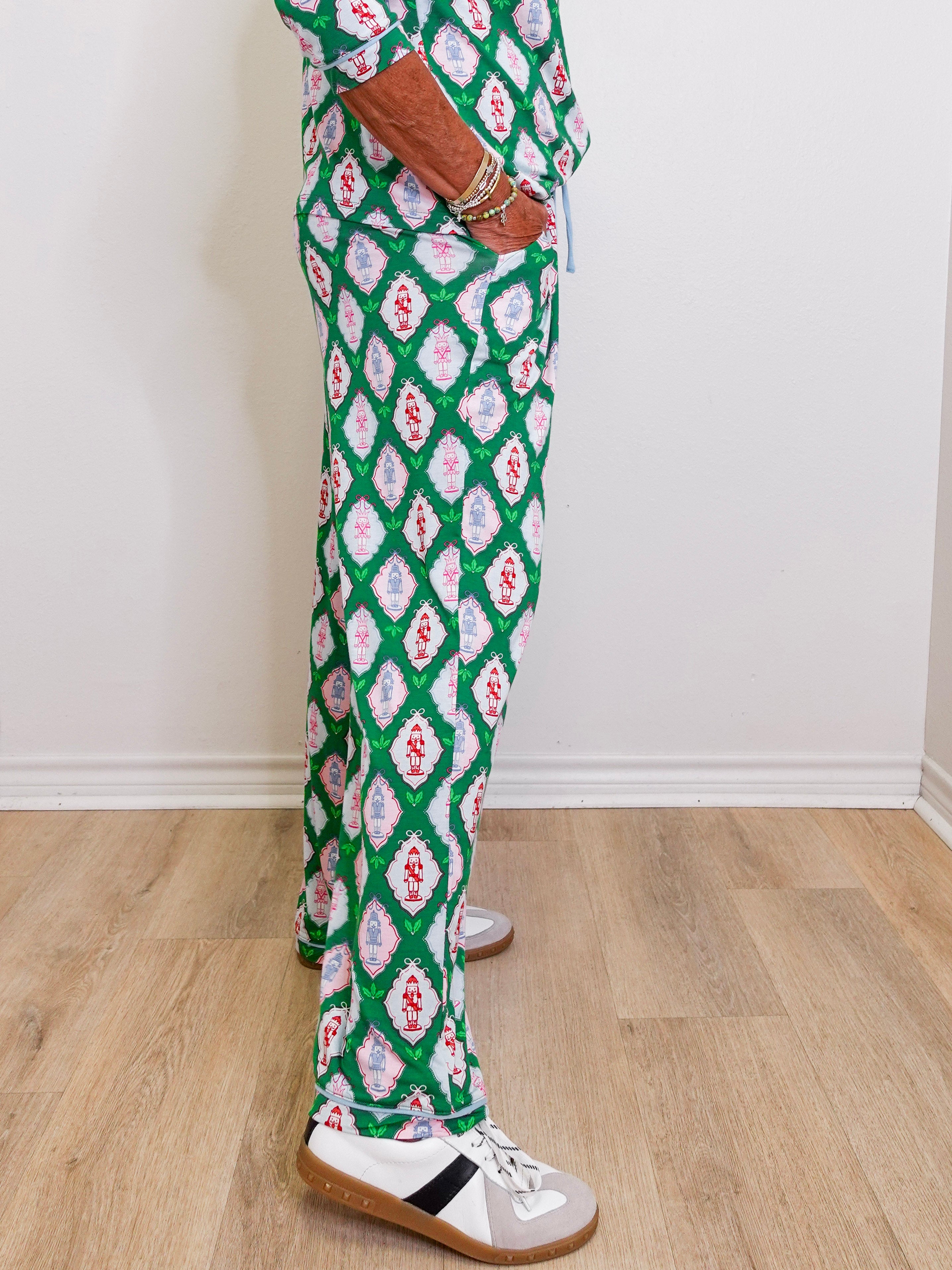 Person wearing green patterned pants with white sneakers on a wooden floor.