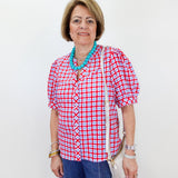 Woman wearing a red and white checkered shirt with a blue necklace against a white background