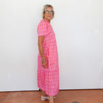 Woman wearing a pink patterned dress standing against a white wall.