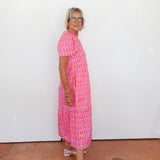 Woman wearing a pink patterned dress standing against a white wall.