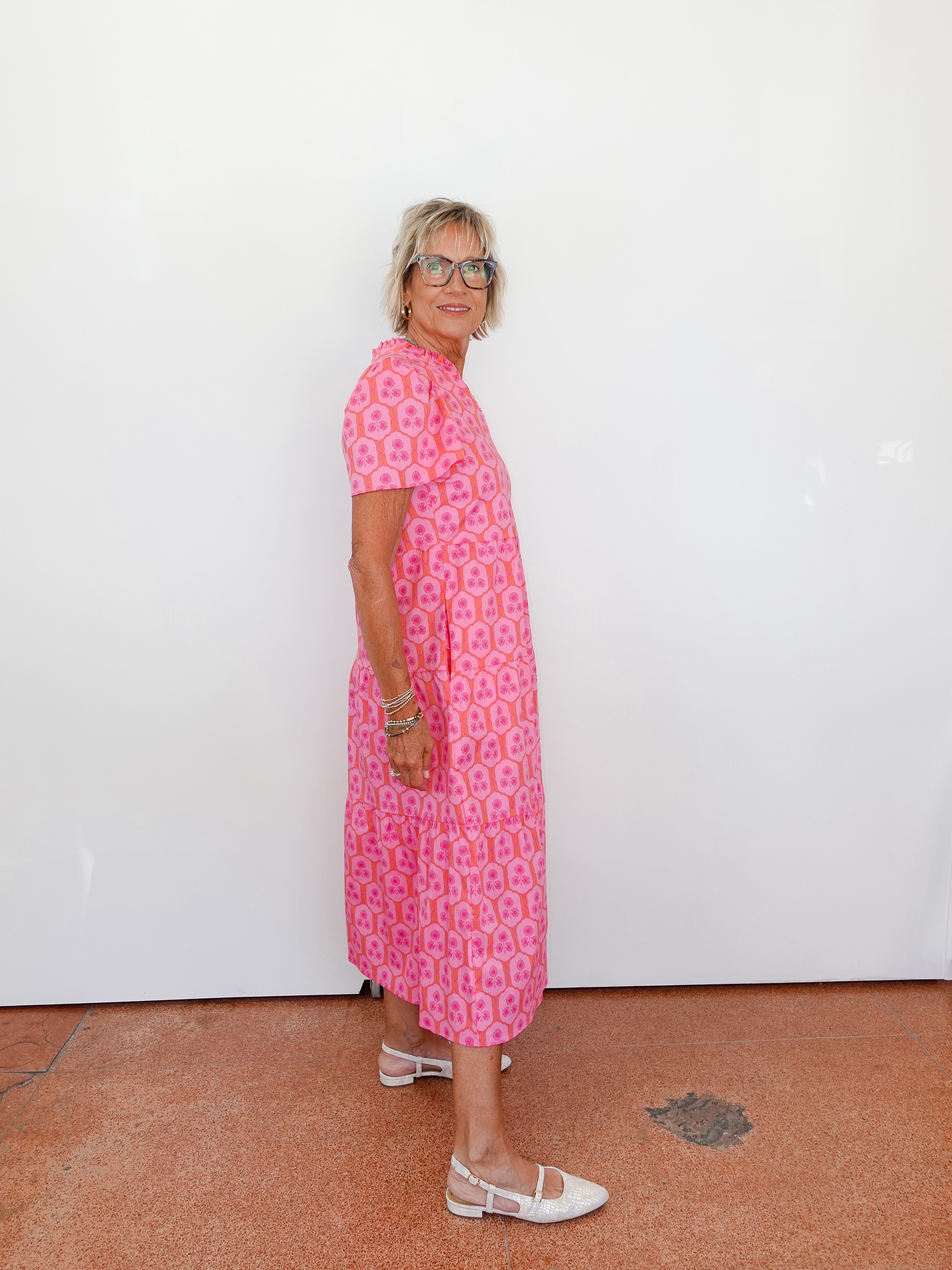 Woman wearing a pink patterned dress standing against a white wall.
