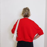 Person wearing a red sweatshirt and black pants against a white wall