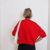 Person wearing a red sweatshirt and black pants against a white wall