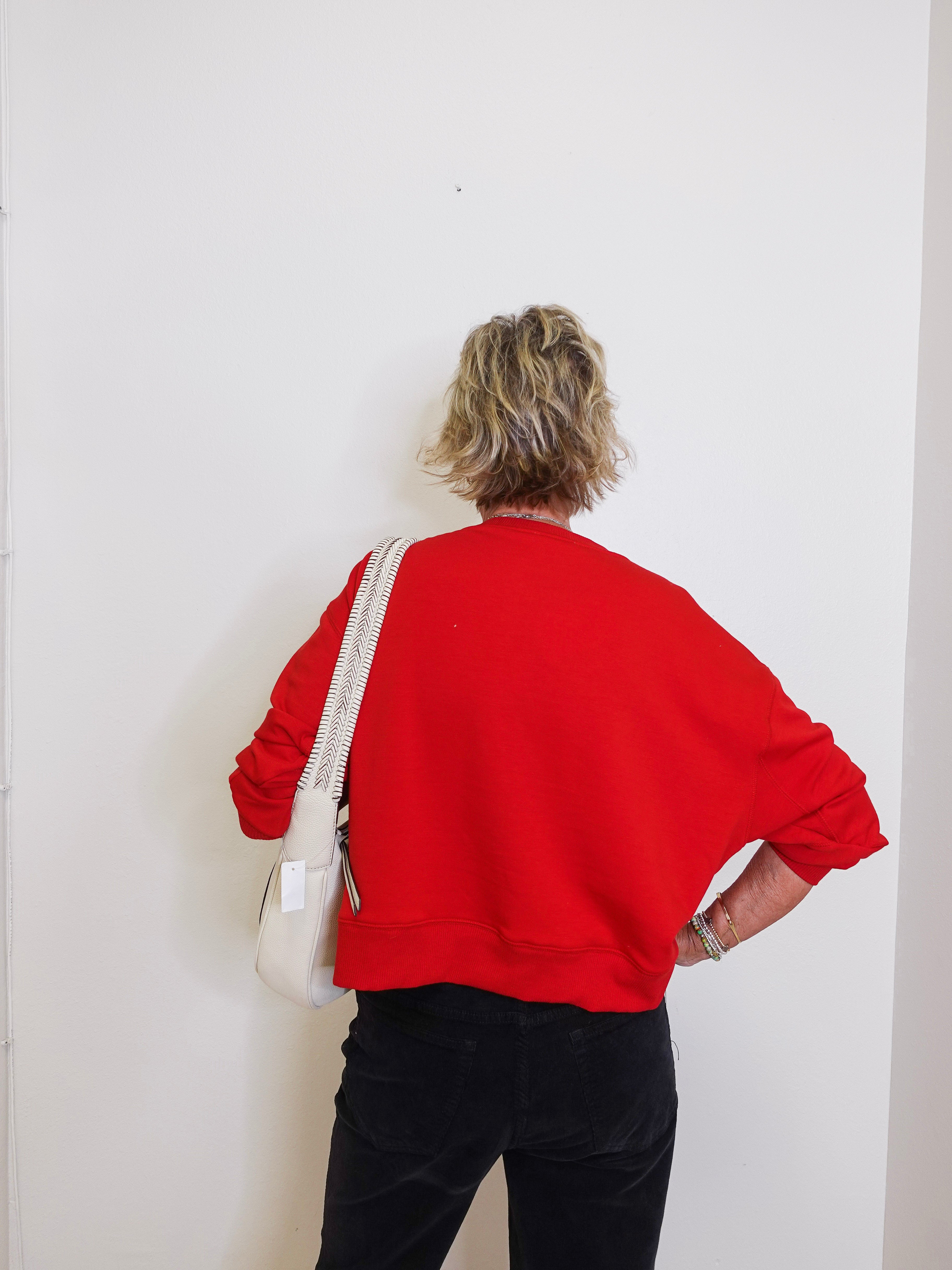 Person wearing a red sweatshirt and black pants against a white wall