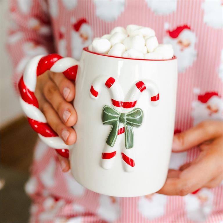Person holding a mug with candy cane handles and marshmallows, wearing festive pajamas.