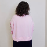 Person wearing a light pink sweatshirt with dark hair against a white wall