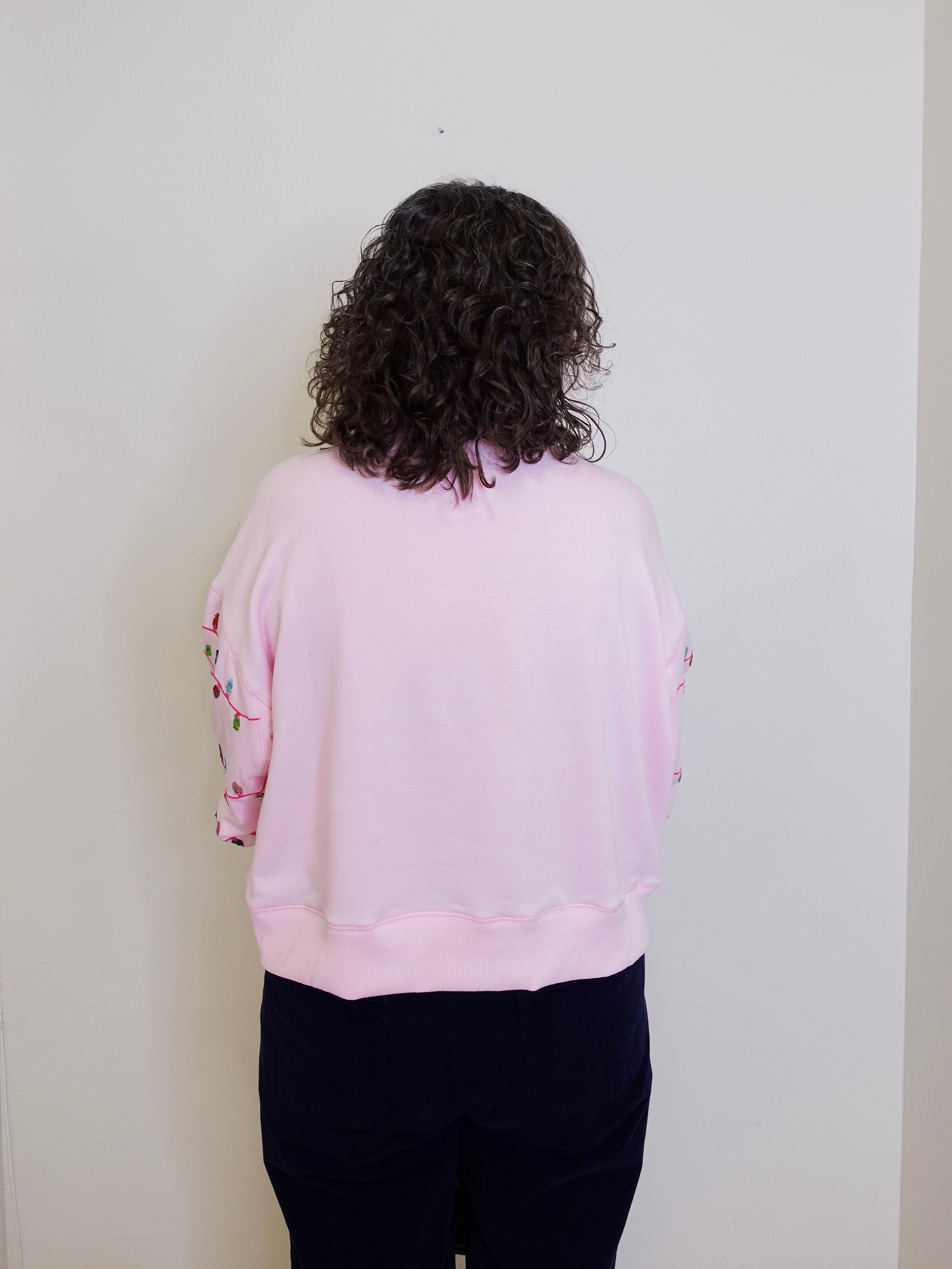 Person wearing a light pink sweatshirt with dark hair against a white wall