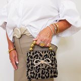 Person holding a leopard print handbag with decorative bow and gold accents.