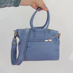 Blue handbag held by a person against a white background