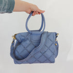 Blue quilted handbag held by a person against a white background