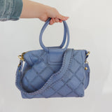 Blue quilted handbag held by a person against a white background