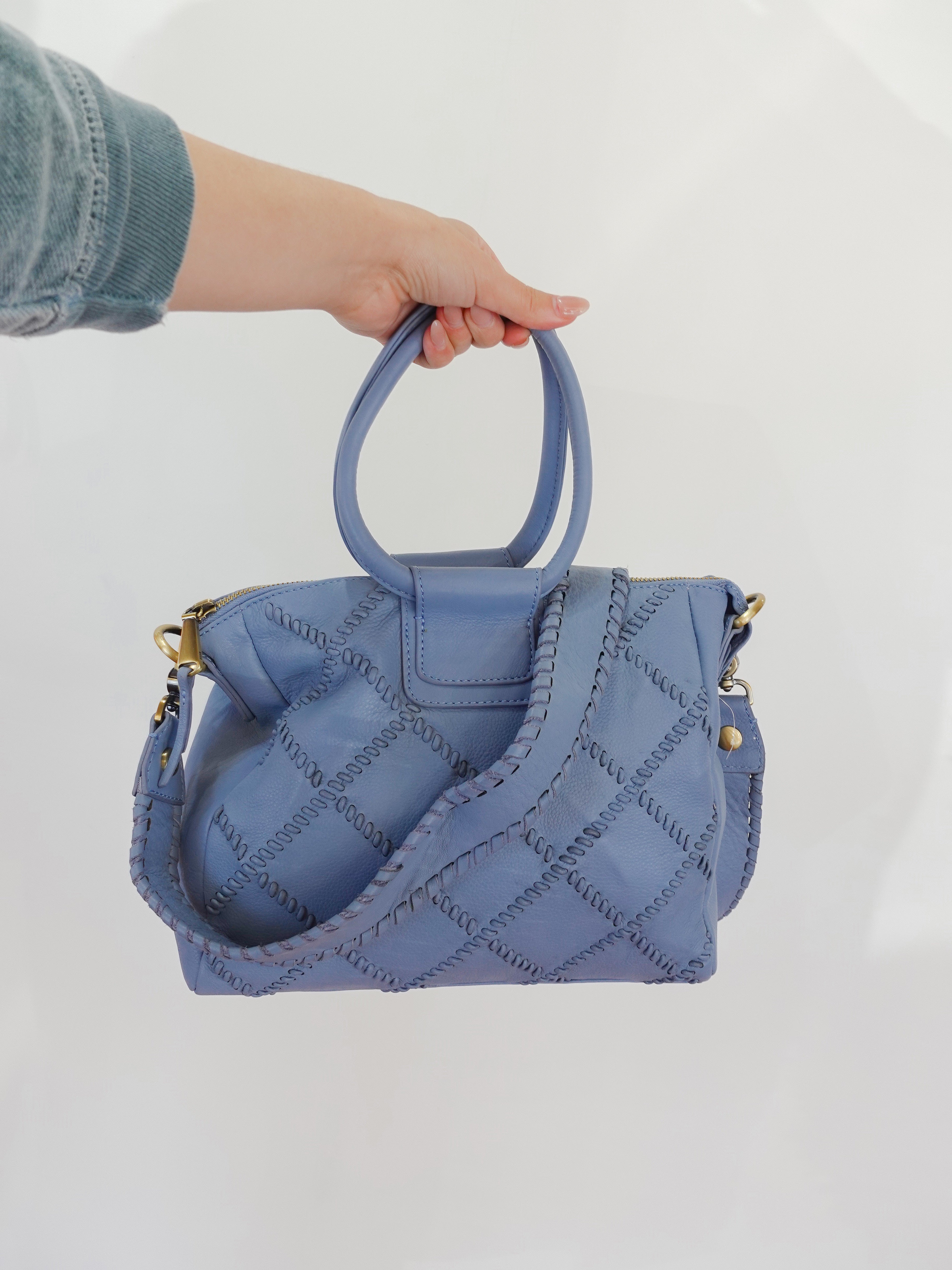 Blue quilted handbag held by a person against a white background