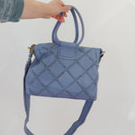 Blue quilted handbag held by a person against a white background