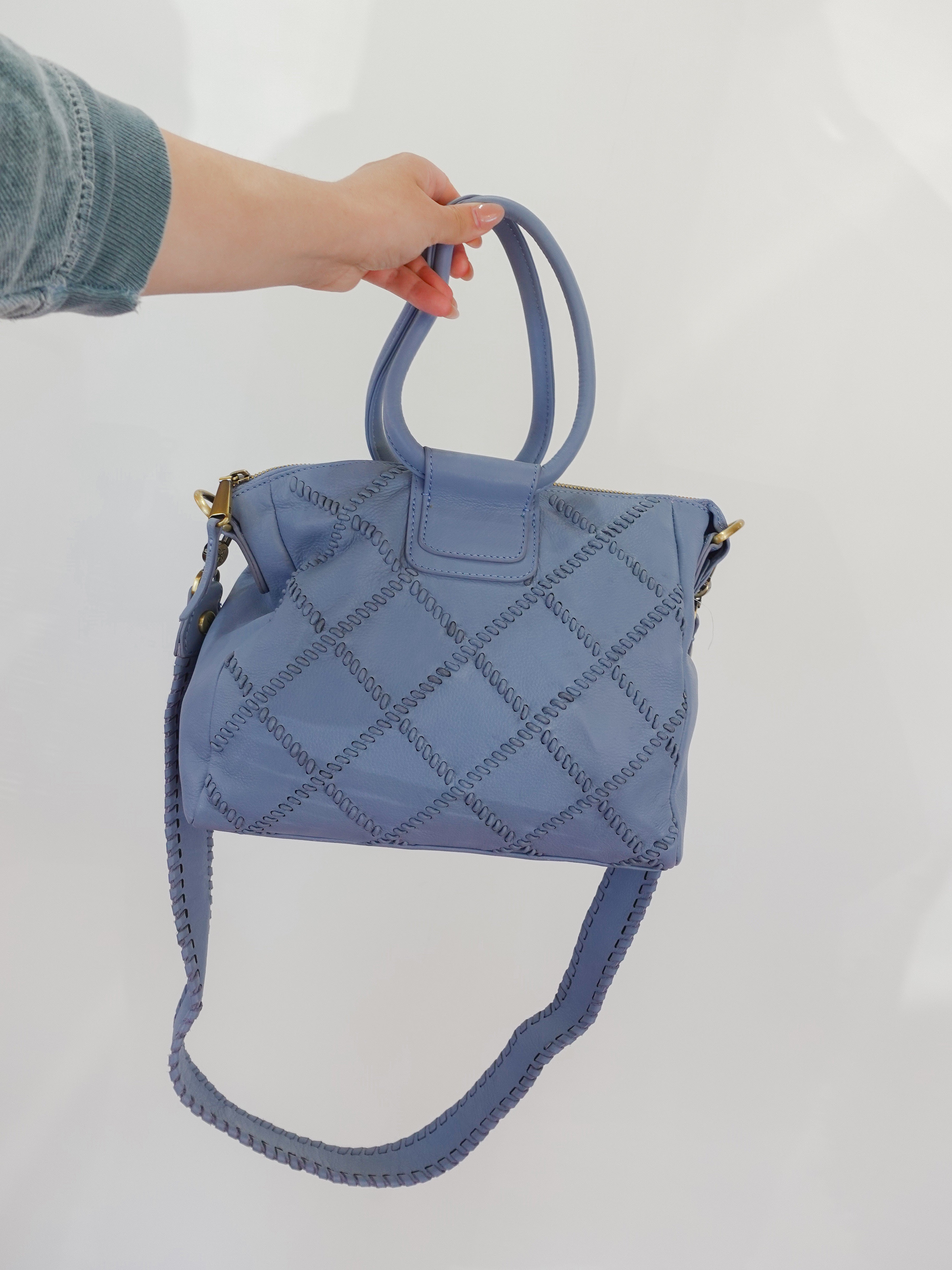 Blue quilted handbag held by a person against a white background
