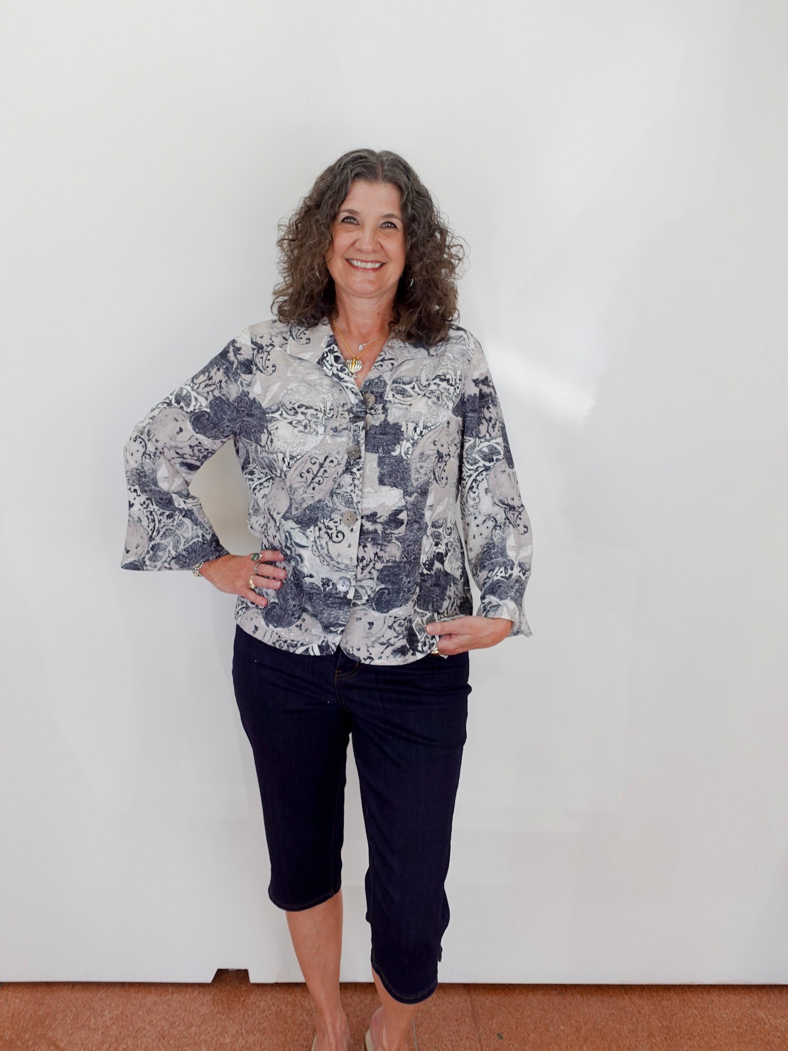 Woman wearing a floral blouse and dark pants against a white wall