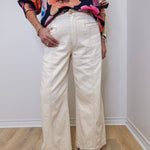 Person wearing a colorful floral top and white wide-leg pants against a plain background